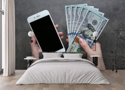 Hands holding smart phone with dollar banknotes on grey background. Making money online Wall mural