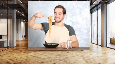 Handsome man eating pasta on table against light background Wall mural