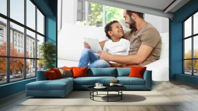 happy father with adopted african-american boy using tablet computer while sitting on couch at home Wall mural