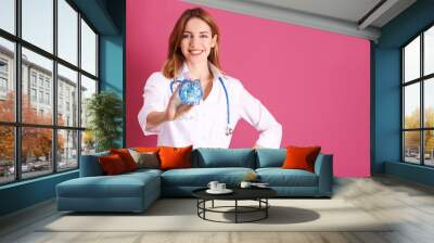 Happy young doctor holding piggy bank on color background Wall mural