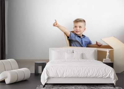 Little boy playing with cardboard box on white wall background Wall mural