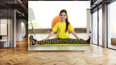 Little cute girl sitting in the splits on a mat indoor Wall mural