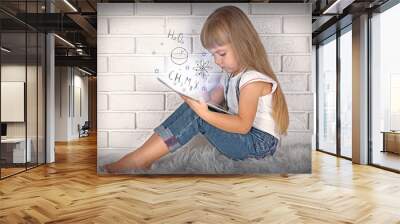 Little girl with tablet on brick wall background. Study and technology concept. Wall mural