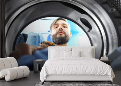 Man doing laundry in laundromat, view from the inside of washing machine Wall mural