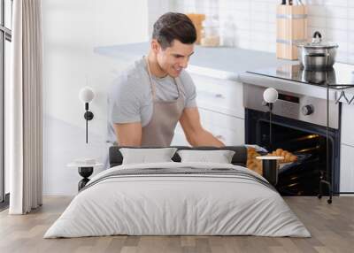 Man taking baking tray with delicious croissants out of electric oven in kitchen Wall mural