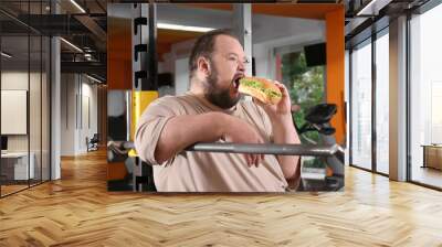 Overweight man eating sandwich in gym Wall mural