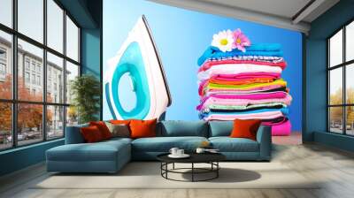 Pile of colorful clothes and electric iron  on blue background Wall mural