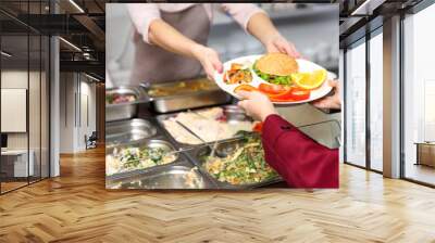 Pleasant woman giving lunch to school girl in cafeteria Wall mural