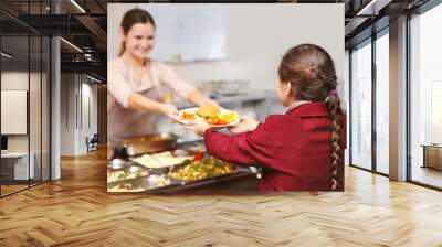 Pleasant woman giving lunch to school girl in cafeteria Wall mural