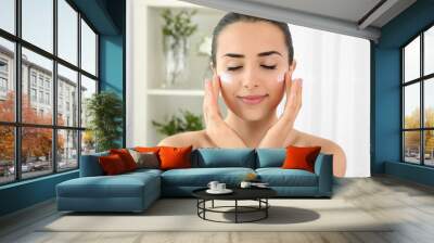 Portrait of young woman applying facial cream Wall mural