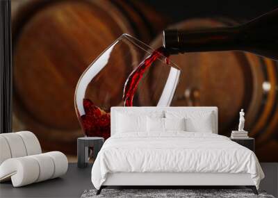 Pouring red wine from bottle into glass with wooden wine casks Wall mural