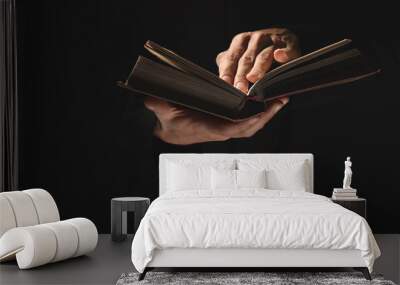 Priest with old Bible on black background, closeup Wall mural