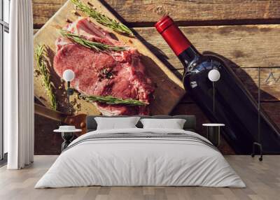 raw pork steak with bottle of red wine, meat fork and rosemary on wooden background Wall mural