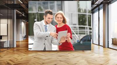 Salesman with tablet and client standing near new car outdoors Wall mural