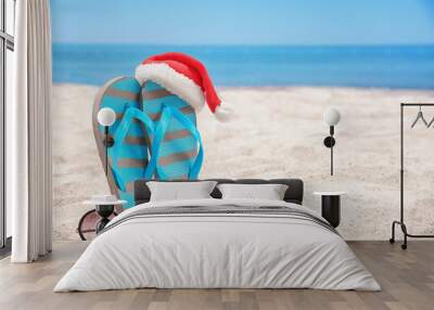 Santa hat with sea star, flip flops and sunglasses on beach. Christmas holidays concept Wall mural