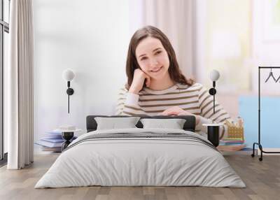 Smiling girl sitting at table with piggy bank and stationery. Saving for education concept Wall mural