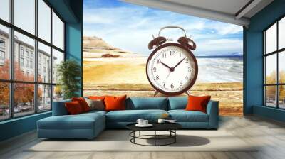 Summer time concept. Alarm clock on wooden table on beach background Wall mural