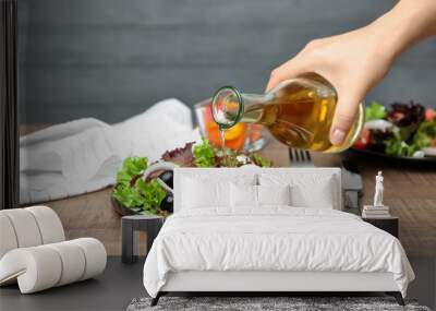 Woman adding tasty apple vinegar to salad with vegetables on table Wall mural