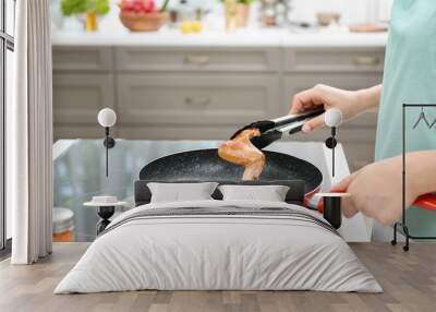 Woman cooking chicken wings in frying pan on stove Wall mural