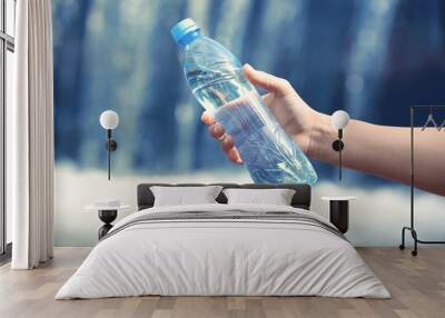 Woman hand holding bottle with fresh water on waterfall  background Wall mural