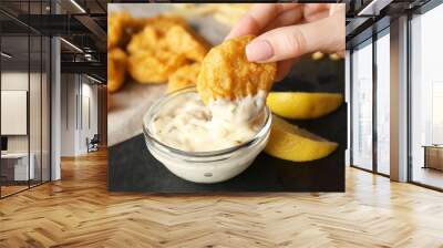 Woman holding tasty nugget and bowl with sauce on table, closeup Wall mural