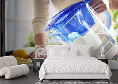 Woman pouring water from filter jug into glass in the kitchen Wall mural