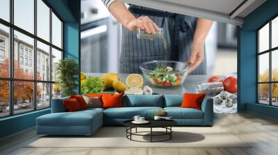 Woman preparing tasty vegetable salad in bowl on table Wall mural