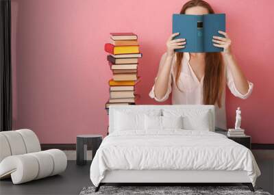 woman sitting on a floor and holding book in front of face on pink background Wall mural