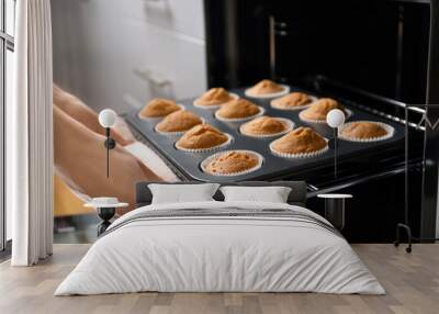 Woman taking baking tray with cupcakes from oven Wall mural