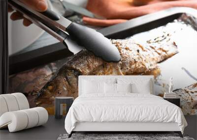 Woman taking tasty fish from baking tray using tongs, closeup Wall mural