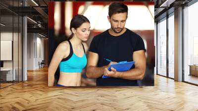 Woman with personal trainer preparing training plan in gym Wall mural