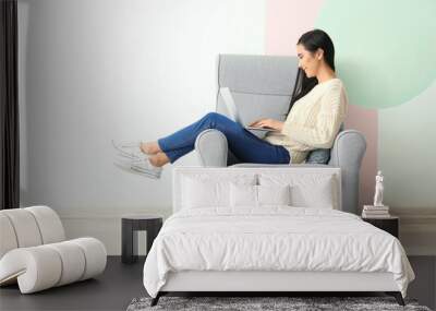 Young Asian woman using laptop in armchair, indoors Wall mural