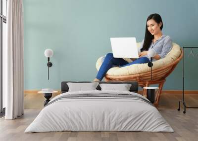 Young Asian woman using laptop in lounge chair, indoors Wall mural