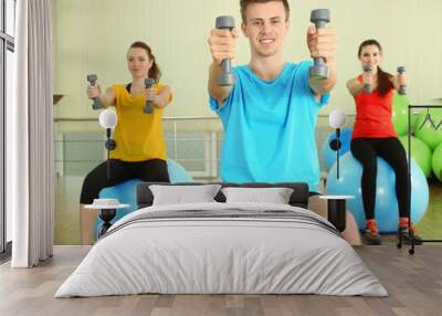 Young beautiful peoples engaged with dumbbells in gym Wall mural