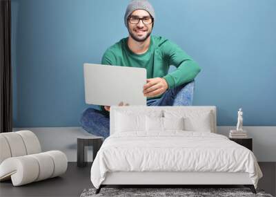 Young blogger with laptop sitting against color wall Wall mural