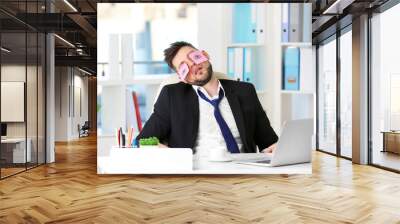 Young business man with fake eyes painted on paper stickers sleeping at workplace in office Wall mural