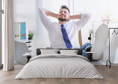 Young businessman relaxing at workplace with his feet on desk Wall mural