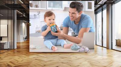 Young dad giving water to his little son at home Wall mural