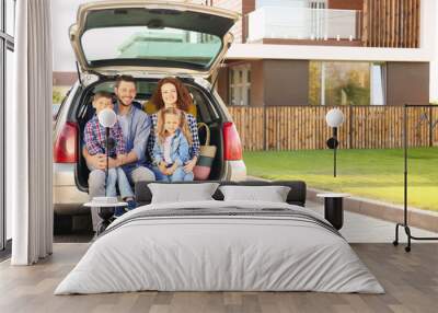 Young family with children sitting in car trunk near house Wall mural