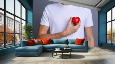 Young man holding red heart on color background Wall mural