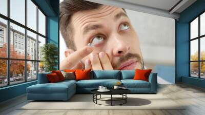 Young man putting contact lenses at home, closeup Wall mural