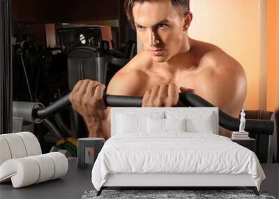 Young man training on exercise machine in gym Wall mural