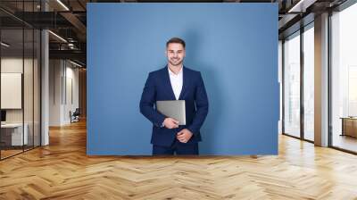 Young man with laptop against blue background Wall mural