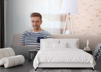 Young man with laptop on sofa in the room Wall mural