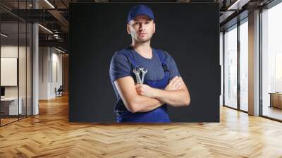 Young mechanic in uniform with crossed arms and wrench standing on a black background Wall mural