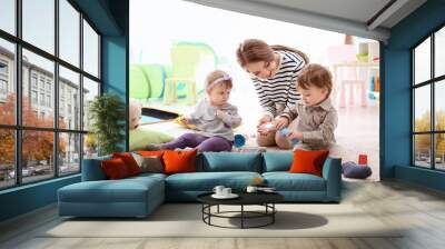 Young nanny playing with little children, indoors Wall mural