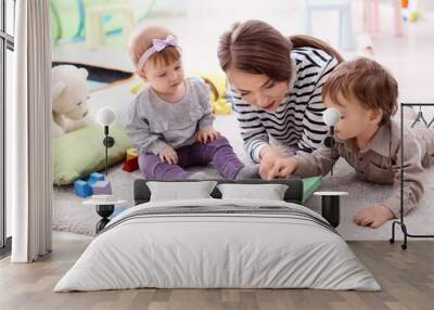 Young nanny with cute little children, indoors Wall mural