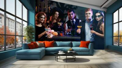 Young people in different costumes drinking cocktails at Halloween party Wall mural