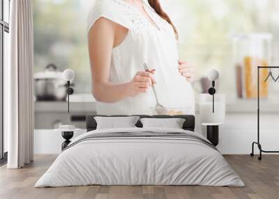 Young pregnant woman eating corn flakes with milk at kitchen, closeup Wall mural