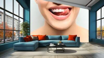 Young smiling woman licking her teeth on light background, closeup Wall mural